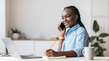 Milenyum Siyahi Kadın Yöneticisi ofisteki cep telefonundan not alıyor ve konuşuyor, tüketicilerle, boş alanlarla konuşuyor.