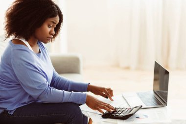 Hesap makinesi kullanan ve kağıtlara bakan, seçici odaklı şaşırmış siyahi kızın yan görünüm portresi