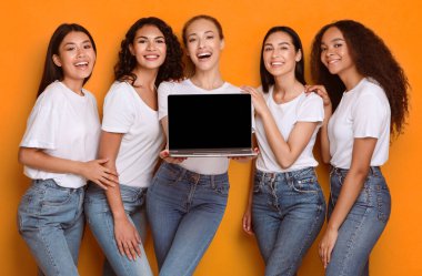 Beş çok ırklı kadın ellerinde dizüstü bilgisayarlarıyla boş bilgisayar ekranı ile sarı stüdyo arka planında duran kızlara yönelik bir web sitesi öneriyorlar. Model