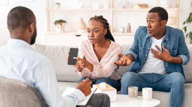 Kıskanç eş. Öfkeli Siyah Kadın, kocalarına telefon gösteriyor, onu aldatma ve sadakatsizlikle suçluyor, Psikiyatristler Ofisi 'ndeki Aile Terapisi oturumunda oturuyor,