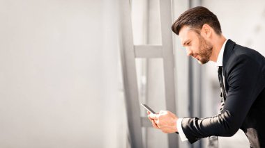 Yakışıklı iş adamı havaalanından ayrılmayı beklerken sevgilisine mesaj atıyor, cep telefonu kullanıyor, yakın plan, kopyalama alanı olan panorama kullanıyor. Siyah takım elbiseli, akıllı telefonlu orta yaşlı girişimci.