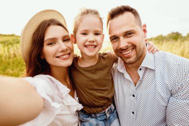 Sevdikleriyle Selfie. Tatlı bir anne, yaz şapkası takmış, çocuğu ve kocasıyla fotoğraf çekiyor, dışarıda birlikte vakit geçiriyor.