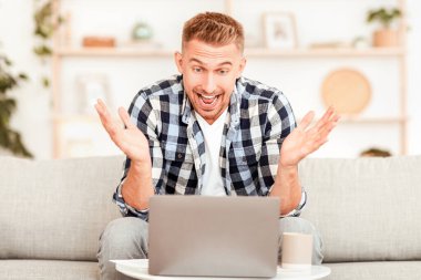 Online Win Concept. Mutlu, heyecanlı adamın portresi başarısını kutluyor oturma odasında kanepede oturuyor, sevinçten bağırıyor, dizüstü bilgisayara bakıyor, boş alana bakıyor. Bilgisayar kullanan harika bir adam.