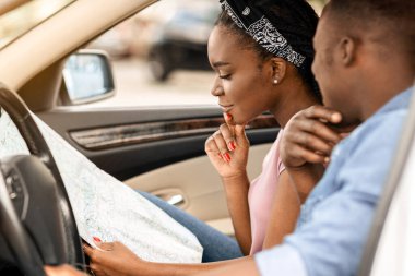 GPS, konum, harita, navigasyon konsepti. Kafası karışmış genç siyah aile arabayla seyahat ediyor, kayboluyor, kağıt haritasını kontrol ediyor, varış, yan görüş, kopyalama alanı arıyor.