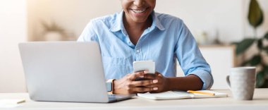 Gülümseyen Afro-Amerikan iş kadını iş yerinde akıllı telefon kullanıyor, mesaj atıyor, internette geziniyor ya da yeni uygulamaları kontrol ediyor, yer kopyalıyor.