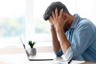 Stresli erkek serbest çalışan ofis masasında oturuyor, kafaya dokunuyor, iş sorunları yaşıyor ya da bilgisayarla çevrimiçi proje üzerinde çalışırken ilham eksikliği yaşıyor, kopyalama alanı ile yan görünüm