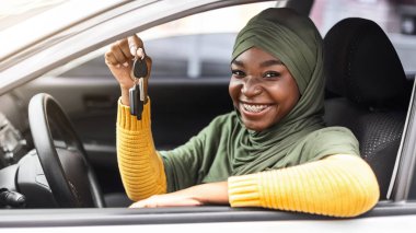 Yeni araba alıyorum. Otomobilinin anahtarlarını gösteren mutlu siyah Müslüman kadın, oto kiralama servisini kullanıyor, sürücü ehliyetini kutluyor, gülümsüyor ve kameraya bakıyor.