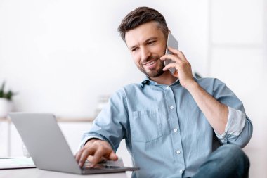 Cep telefonu ve dizüstü bilgisayarla uzaktan kumandayla çalışan neşeli genç adam, masada oturuyor, boşluğu kopyalıyor.