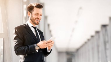 Havalimanında uçuş beklerken sevgilisiyle sohbet eden şık takım elbiseli neşeli iş adamı, cep telefonu kullanıyor, fotokopi çekiyor. Mutlu girişimci, iş ortaklarından gelen e-postaları okuyarak iyi haberler aldı.