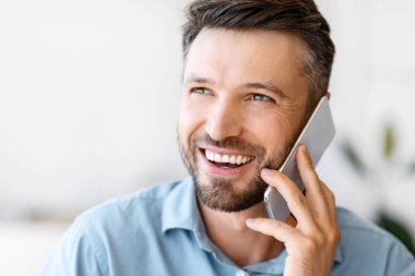 Kapalı alanda cep telefonuyla konuşan gülümseyen genç iş adamının yakın plan portresi.