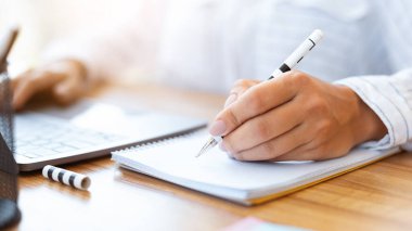 Kişisel Planlayıcı. Tanımlanamayan kişi not defterine yazıyor. Çalışma yerinde oturuyor, notlar alıyor, plan yapıyor.