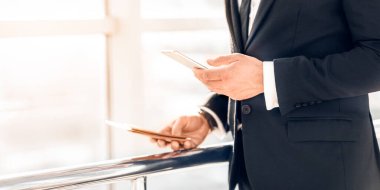 Telefon kullanan, pasaport ve uçak biletlerini elinde tutan, havalimanının penceresinde bekleyen, kalkışı bekleyen tanınmamış iş adamlarının yakın çekimi. Kopya alanı. Takım elbiseli adam cep telefonundan e-postayı kontrol ediyor