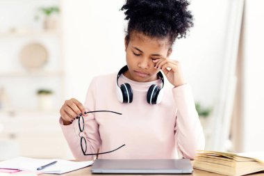 Görme problemi. Yorgun siyah genç kız, Aching Eye 'a dokunuyor, elinde gözlük, dizüstü bilgisayarında oturuyor.
