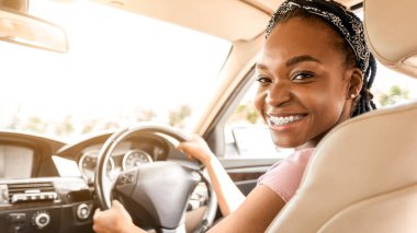 Lüks araba kullanan, kameraya gülümseyen kendine güvenen genç siyahi kadın, yakın çekim, kopyalama alanı. Heyecanlı afro-amerikan bayan sürücü en yeni arabasını test ediyor, direksiyonun başında oturuyor.