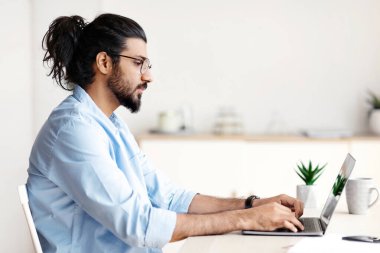 Serbest meslek hayatı. İçişleri Bakanlığı 'nda dizüstü bilgisayarda çalışan bin yıllık Arap adam, masa başında oturan ve bilgisayar klavyesinde yazan genç Doğulu adam, çevrimiçi proje üzerinde çalışıyor, boş alanla yan görünüm