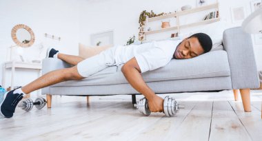Yorgun, Afro-Amerikan bir adamın evde antrenman yaptıktan sonra koltukta uzanarak uyuması. Sportif Yaşam Tarzı, Sportif Başlangıç Zorlukları. Panorama