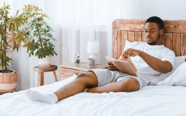 Daha fazla oku. Afro-Amerikalı Adam en çok satanlar kitabını okuyor. Evdeki yatak odasında rahat bir şekilde uzanıyor. Siyah adam Tembel Sabahın tadını çıkarıyor. Haftasonu Dinlenme ve Dinlenme Konsepti