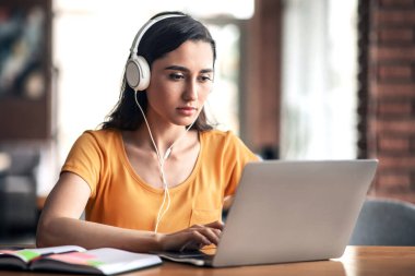 Konsantre olmuş Arap kız klavyede daktilo çalıyor, kafede ders çalışıyor, kulaklık takıyor.