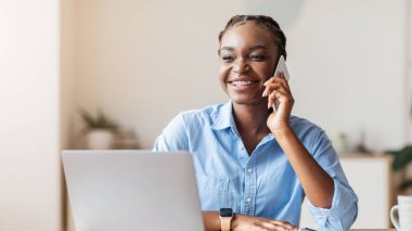 Ofiste cep telefonuyla konuşan genç siyahi bir girişimci müşteriye danışıyor, gülümsüyor ve başka yöne bakıyor.