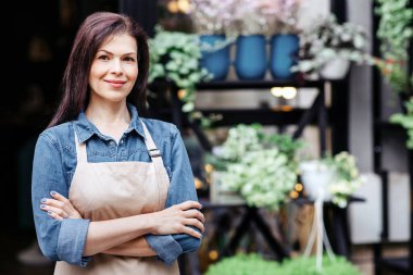 Kendine güveni olan küçük işletme sahibi, çevreci kafe garsonu ve çiçekçi müşterileri bekliyor. Önlüklü, gülümseyen, çekici bir bayan göğsünde, bitkilerin arka planında, fotokopi odasında kollarını açtı.