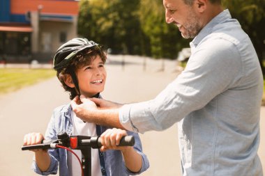 Parktaki kıvırcık çocuğa koruyucu miğfer takan yetişkin bir adamın portresi. Bisiklete biniyor, geçmişi bulanık.