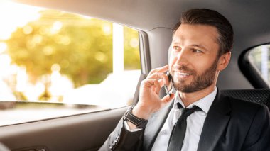 Neşeli CEO ya da yönetici arabasıyla havaalanına giderken cep telefonuyla konuşuyor, açık pencereden bakıyor. Mutlu iş adamı arabada otururken iş konuşuyor, boşluğu kopyalıyor.