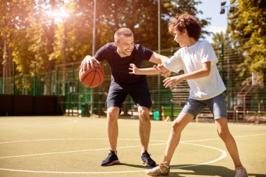 Spor Eğitim Konsepti. Erkek ve kıvırcık çocuk güneşli bir günde basketbol oynuyorlar, topa liderlik ediyorlar.