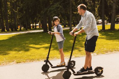 Bağlanma kavramı. Babası, neşeli oğluyla e-scooter 'a binip parka gitmiş.