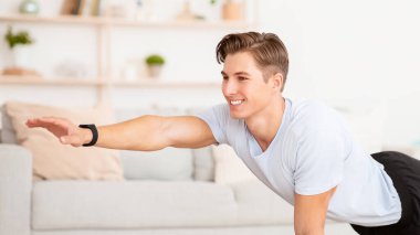 Evde uzaktan antrenman. Spor kıyafetli gülümseyen adam paspasın üzerinde eller için egzersiz yapıyor.
