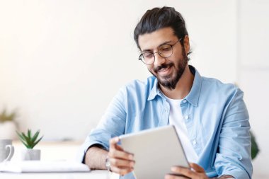 Arap Serbest Çalışan Adam 'ın evde dijital tablet kullanması, işe ara vermesi, masa başında oturması, internete veya sosyal medyaya bakması, yeni uygulamalara bakması, Doğulu Adam Mesajlaşması ya da İnternet' te alışveriş yapması.