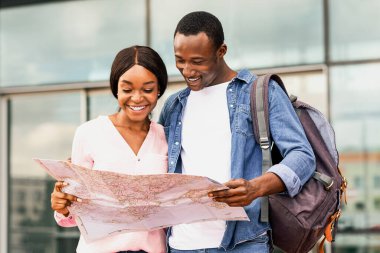 İki mutlu siyah turist havalimanına yakın duruyor, şehir haritasını kontrol ediyor, neşeli Afrikalı Amerikalı erkek ve kadın planlama rotası, heyecanlı milenyum çifti birlikte seyahatin tadını çıkarıyor,