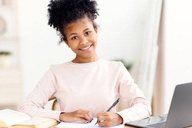 Ev Eğitimi. Ev ödevi yapan, odasında masa başında oturan ve kameraya gülümseyen tatlı bir kız.