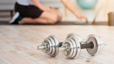 COVID-19 'da kalırken egzersiz. Dambıllar yaklaşın, genç adam hasırda oturuyor ve spor malzemeleriyle dizüstü bilgisayarda çalışıyor.