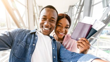 Havalimanında, pasaportlarını, biletlerini ve fotoğraf makinesine birlikte poz verdikleri sırada özçekim yapan heyecanlı siyah çift.