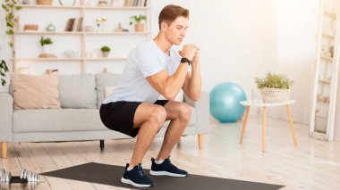 Ev antrenmanı için online koç. Spor giyimli yakışıklı, spor ayakkabılı, spor ayakkabılı, çömelmiş ve oturma odasındaki dizüstü bilgisayara bakan, boş bir yer.
