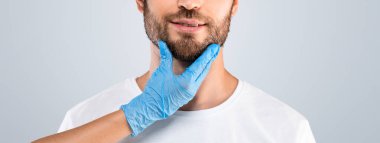 Orta yaşlı, gözleri kapalı bir adam güzellik iğnesi yaptırıyor estetik cerrah ya da hemşire ameliyattan önce hasta yüzüne dokunuyor gri stüdyo arka planı, fotokopi odası. Erkek estetiği kozmetolojisi