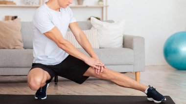 Sabahları covid-19 sırasında esneme ve egzersiz. Spor giyim işindeki kaslı adam oturma odasının içinde paspasın üzerinde çalışıyor.