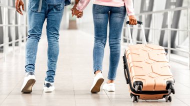 Tatile hazırım. Havaalanı terminalinde bavulları uçuş kapısına giden Afro-Amerikan erkek ve kadının arka görüntüsünde siyah çiftin el ele tutuşurken görüntüsü.,