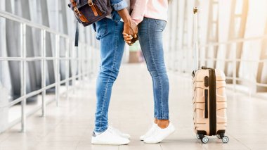 Romantik siyah çift birlikte seyahat ediyorlar, havaalanında el ele tutuşuyorlar, uçuşlarını bekliyorlar, boş alanlı yan görüntü.