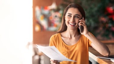 Genç Arap kız telefonda müşteriyle proje tartışıyor, kafede dizüstü bilgisayarla çalışıyor, boşluğu kopyalıyor.