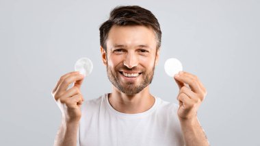 Yüzü için pamuk tutan neşeli sakallı adam gri stüdyo geçmişini temizliyor, boş yer var. Mutlu orta yaşlı bir adam toner ile yüzünü temizliyor. Taze, geveze yüz derisinin tadını çıkarıyor.