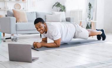 Evde eğitim. Çevrimiçi Antrenman sırasında laptopta Plank Egzersizi Yapan Siyah Adam