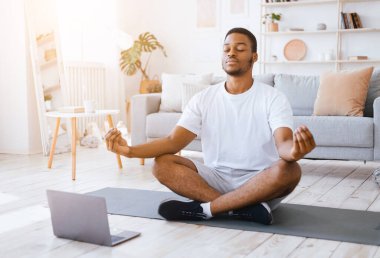 Çevrimiçi yoga. Rahatlamış Afro-Amerikalı Adam dizüstü bilgisayarda meditasyon yapıyor Lotus pozisyonunda oturuyor gözleri kapalı evde dinleniyor. Günlük meditasyon ve rahatlama, sakin olun. Seçici Odaklanma