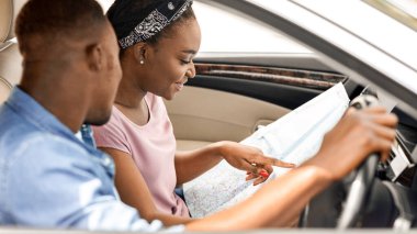 Mutlu siyah çift gezginleri rahat araba kullanırken haritaya bakarlar, yan görüş, kopyalama alanı. Pozitif Afro-Amerikan erkek ve kadın seyahate başlamadan önce haritayı kontrol ediyor, otomatik olarak oturuyor