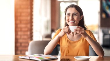 Cafe 'de kahve içen neşeli Arap kız iş fırsatlarını hayal ediyor, boş yere bakıyor.