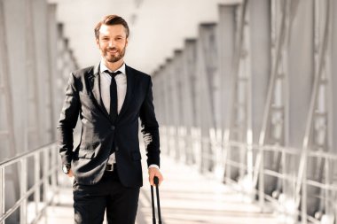 Zengin, orta yaşlı, siyah takım elbiseli, bavullu, havaalanında poz veren, kameraya bakan ve gülümseyen, fotokopi alanı olan bir panorama yöneticisi. İş gezisi, iş seyahati
