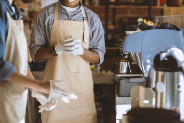 İş gününün başlangıcında, koronavirüs sırasında yeni normal ve küçük işletmeler. Önlüklü genç Afrikalı Amerikalı erkek ve kadın kahve makinesinin yanında koruyucu eldivenler giydiler.