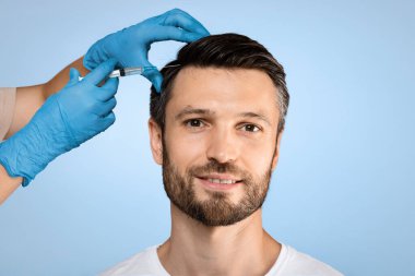 Yakışıklı genç adam kuaförde saç bakımını yaptırıyor, gri stüdyo geçmişi var. Gülümseyen adam güzellik salonunda mezoterapi seansı yapıyor, terapist elinde koruyucu eldivenle şırınga yapıyor.