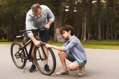Odaklanmış baba ve oğul bisikletlerinin lastiklerini kontrol ediyor, tekerleklere dokunuyorlar.