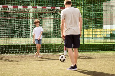 Eşleşme. Birlikte futbol oynayan iki adamın portresi, kalede top bekleyen küçük bir adam.